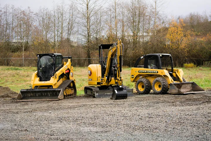 TrackWest's track loader, mini excavator, and skid steer lined up on a gravel lot