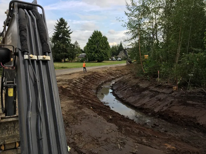 Excavator arm and bucket digging through rocky ground in a ditch near Newport, WA