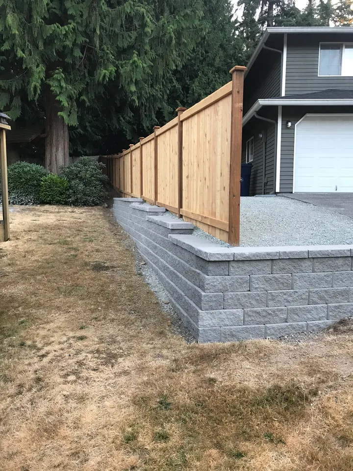 Cedar fence built along the top of a block retaining wall, posts set behind the wall