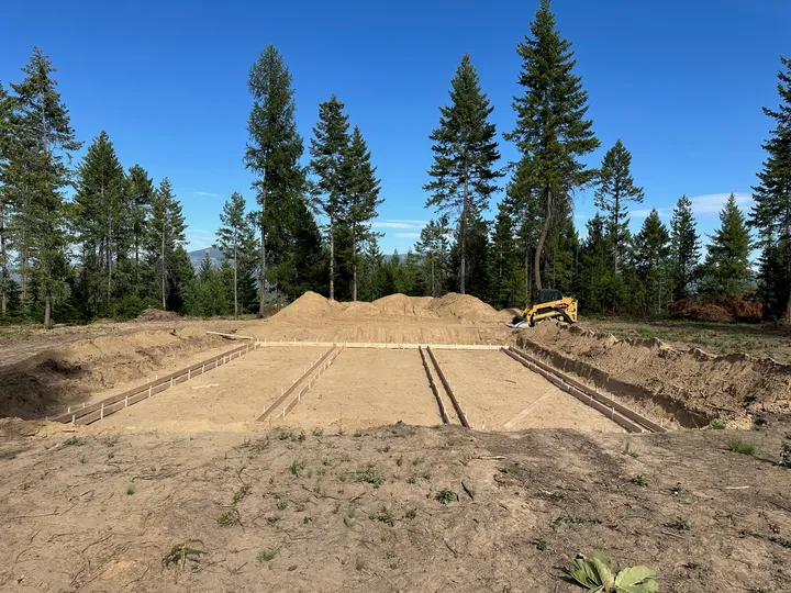 Staked foundation cut with clean banks on a cleared lot surrounded by pines near Newport, WA