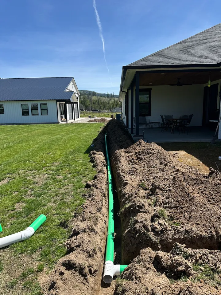 Green septic line laid in an open trench beside a new home before backfill
